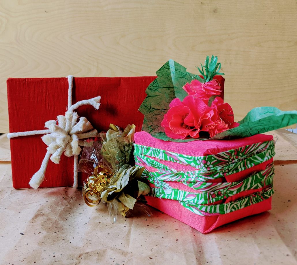 beautifully wrapped gifts, one with red paper and white rope bow and one with neon pink paper and a paper flower on top