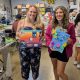 two friends pose holding their art: one is a paint and paper collage, the other is a mixed media collage that says "PLAY"